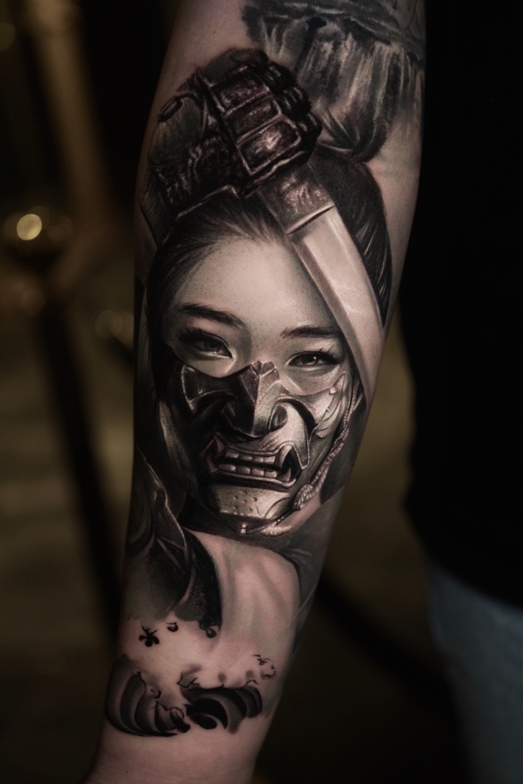 Realistic black and grey tattoo of a geisha with a samurai mask on a forearm