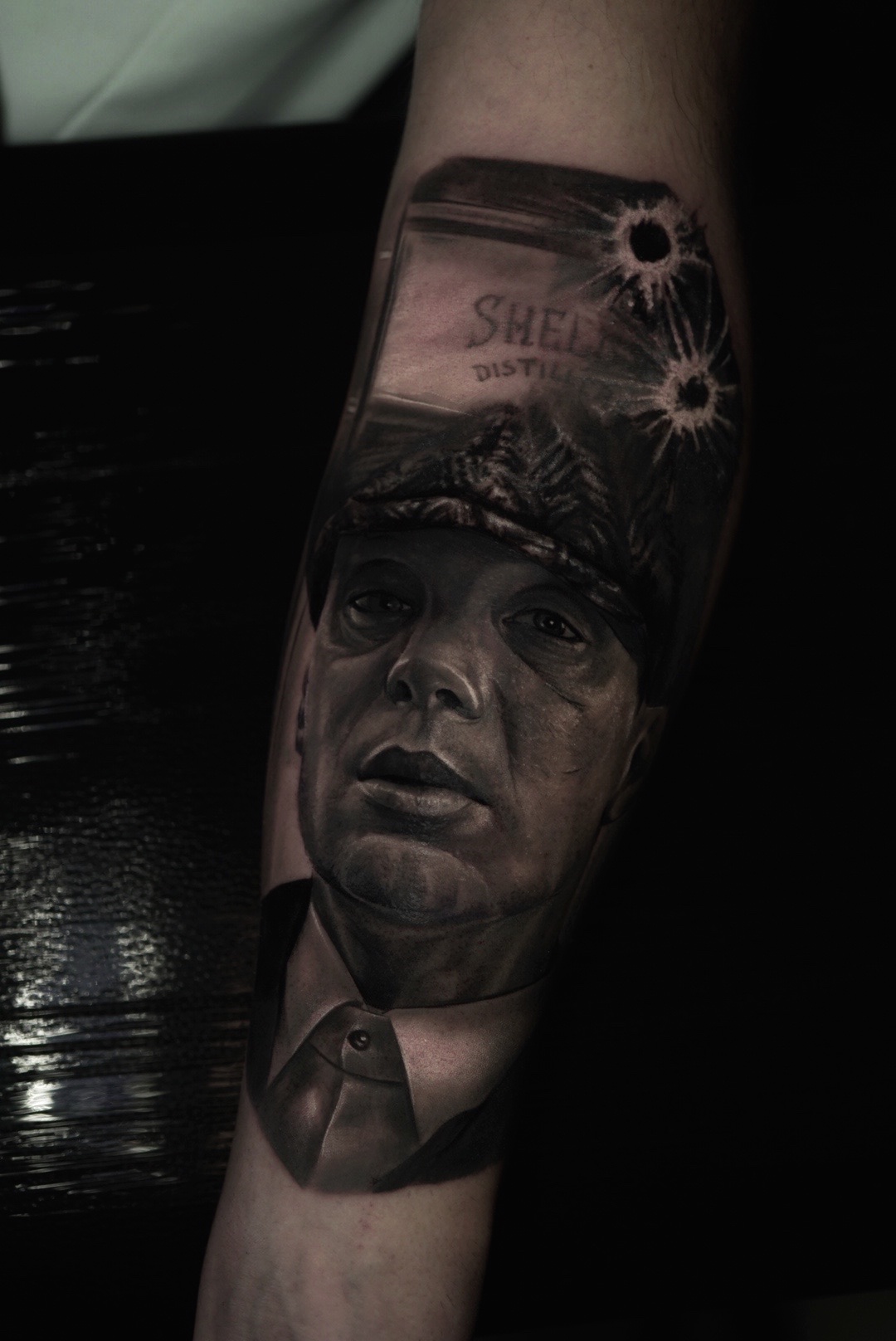 Realistic black and grey portrait tattoo of a man in a cap with a whisky bottle on a forearm