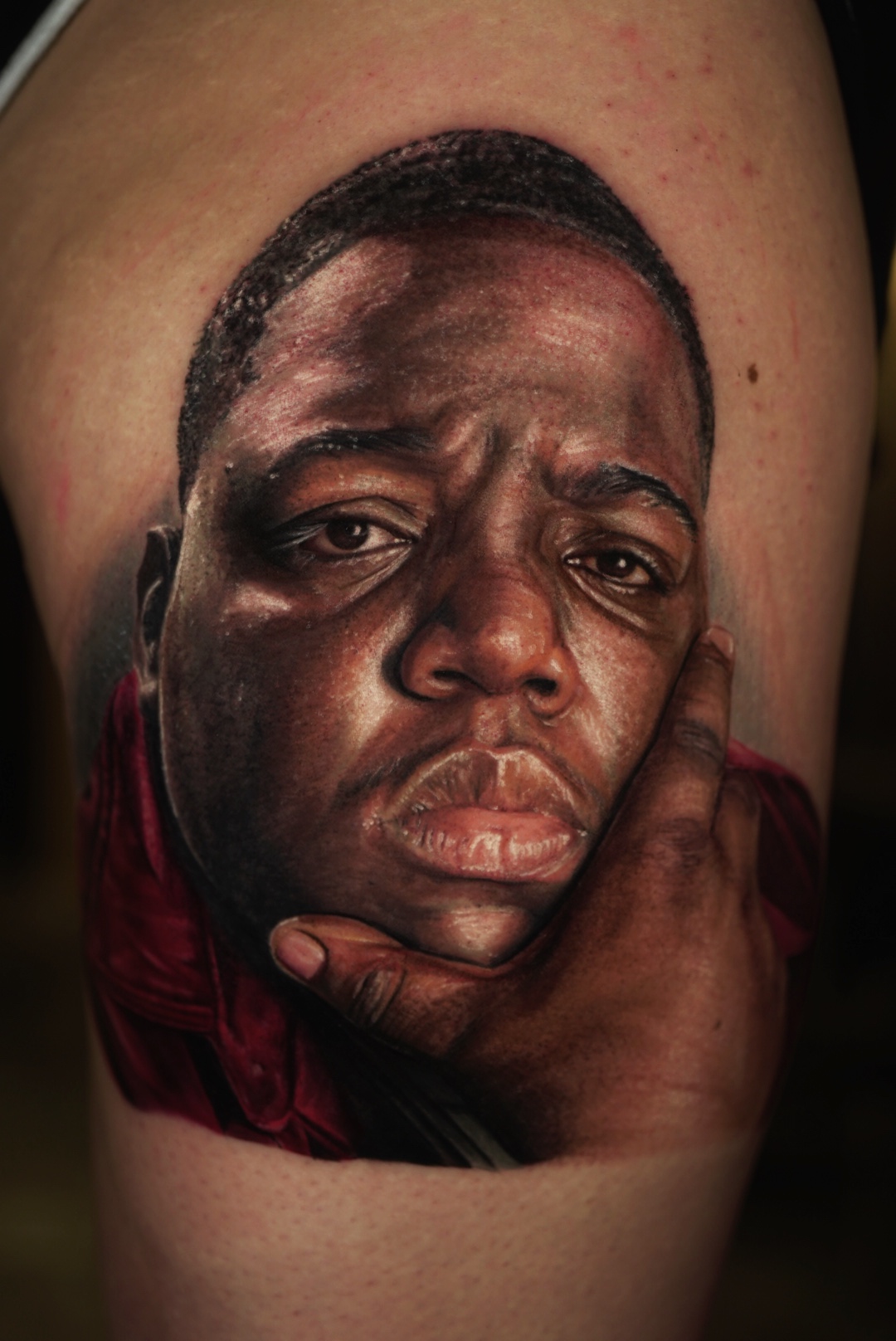 Color realism portrait tattoo of a rapper in a red shirt on an upper arm