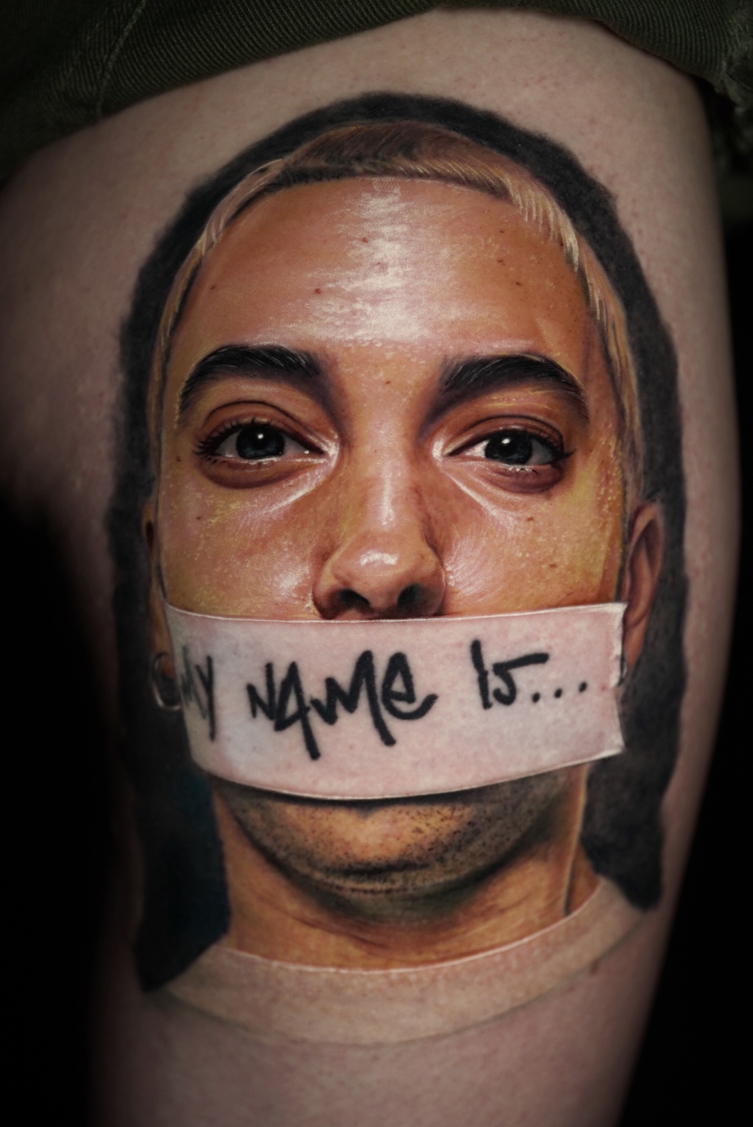 Color realism portrait tattoo of a man with tape over his mouth on a thigh